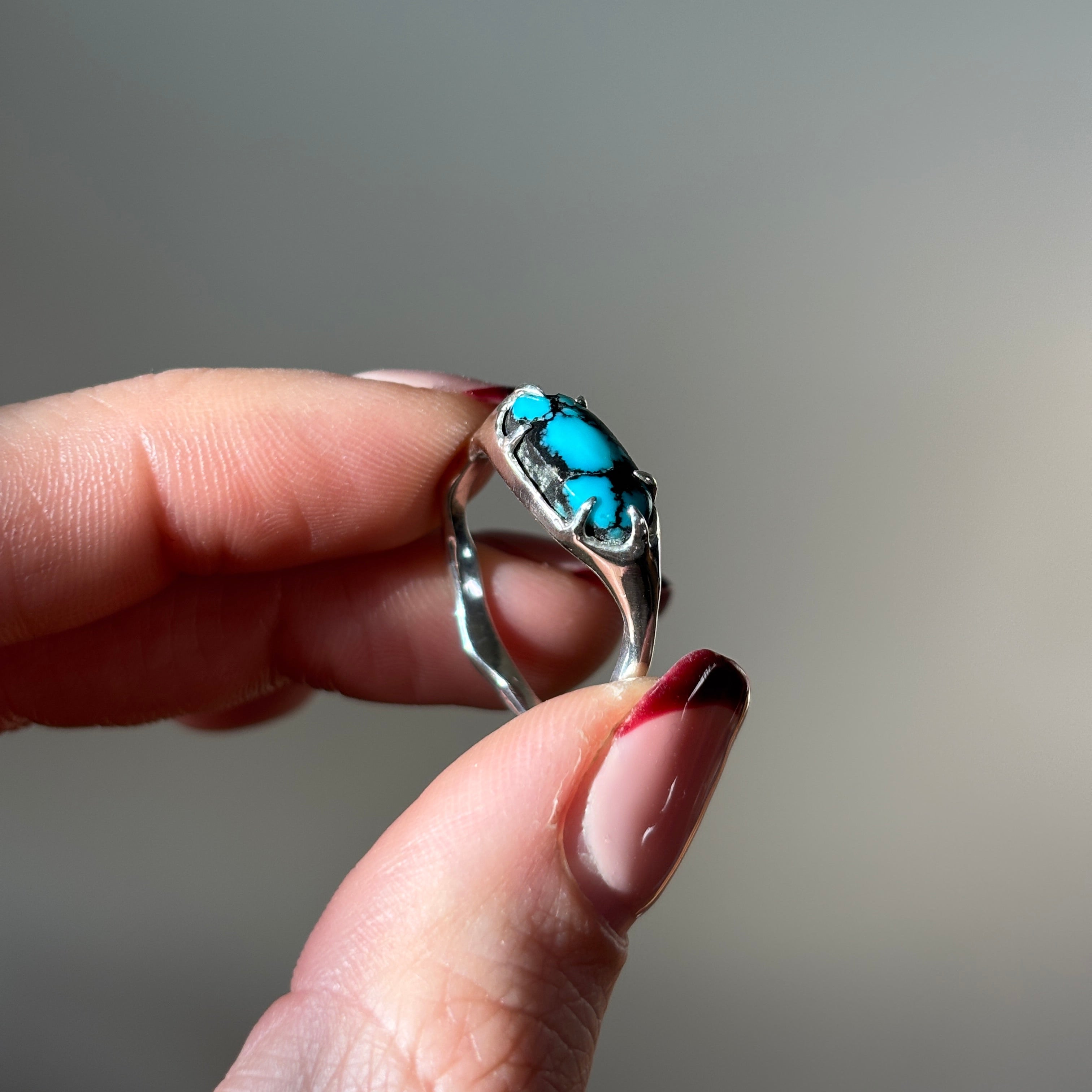 silver and turquoise ring held up in between two fingers.