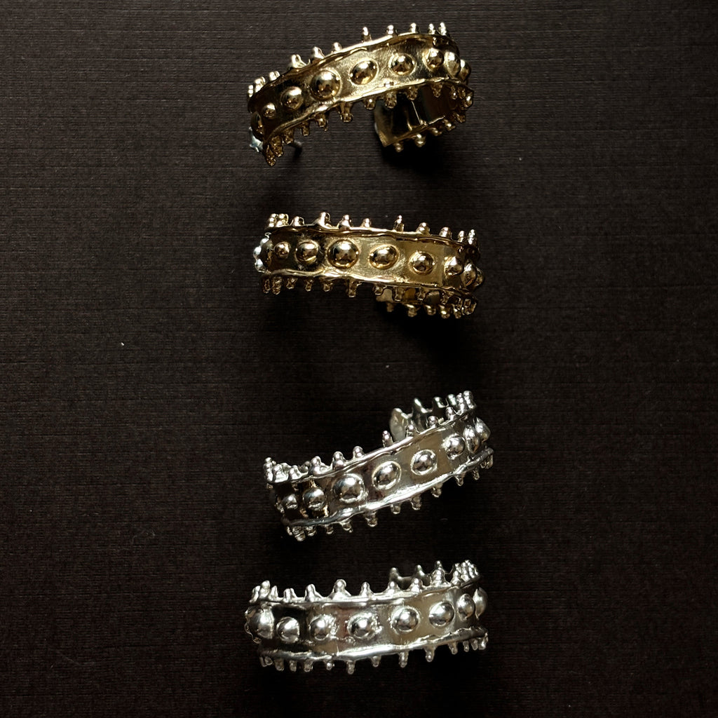 Large chunky textured hoop earrings. Shown in silver and brass on a brown background. 