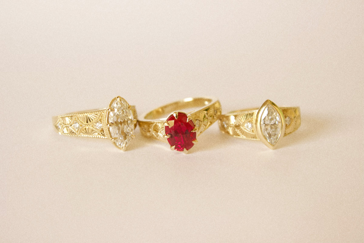 Three vintage-style hand engraved gold rings displayed on a light beige background. 