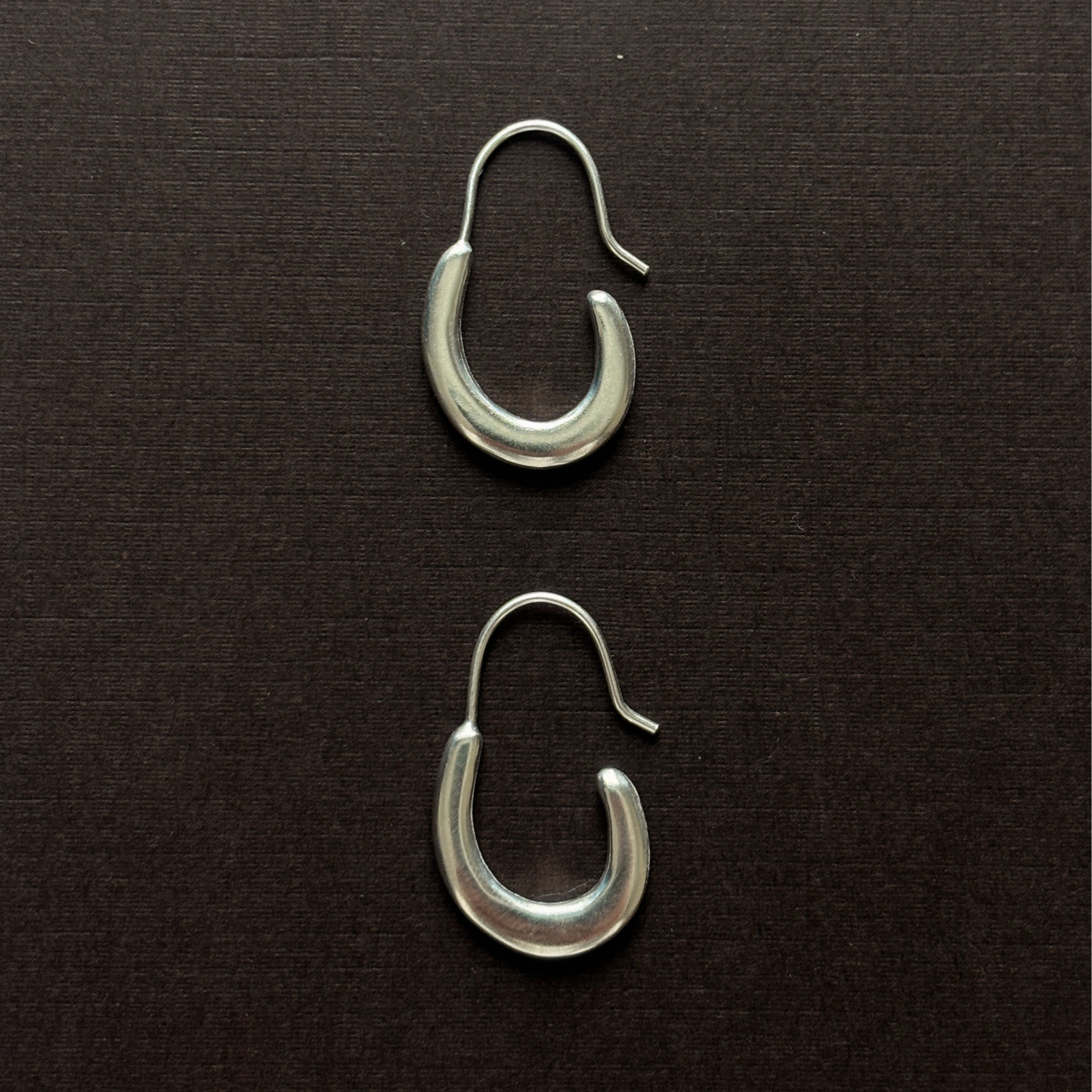 small elongated sterling silver pair of hoop earring on a brown background 