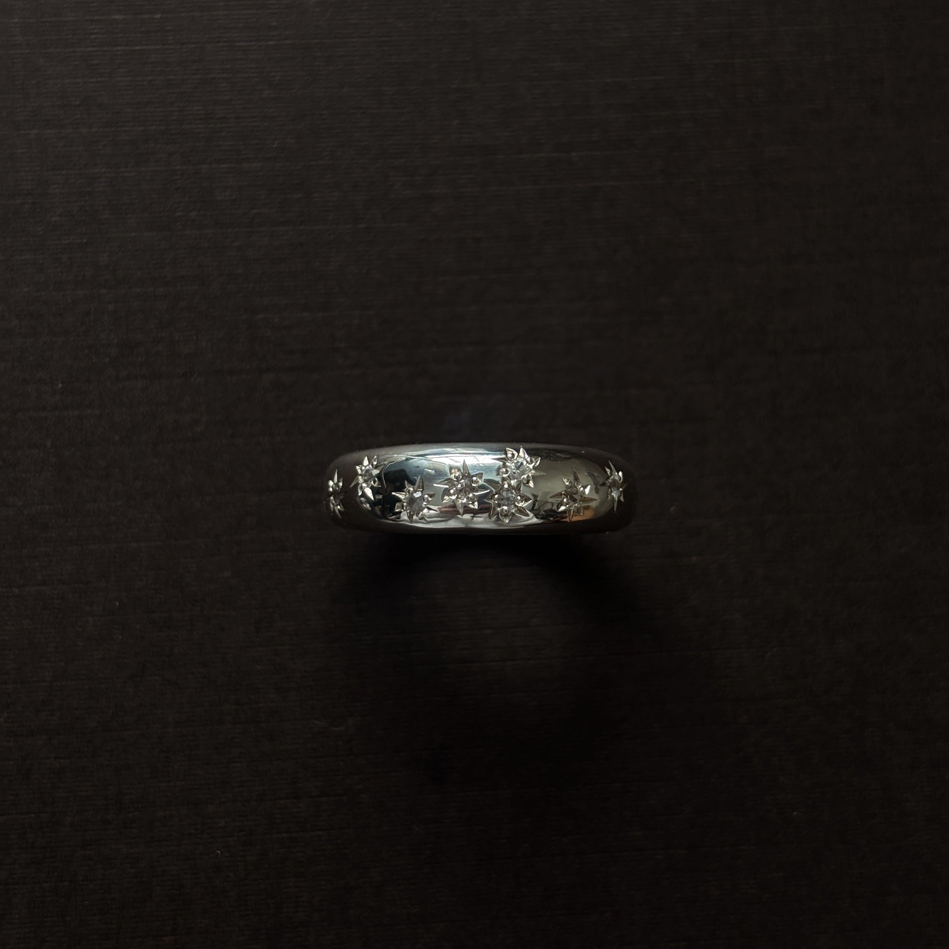 Silver ring with embedded stones on a dark surface