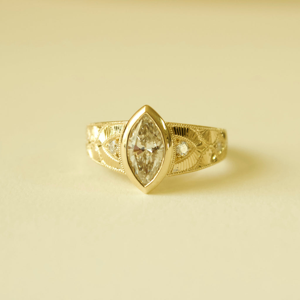 Gold hand engraved bezel marquise ring on a cream background 