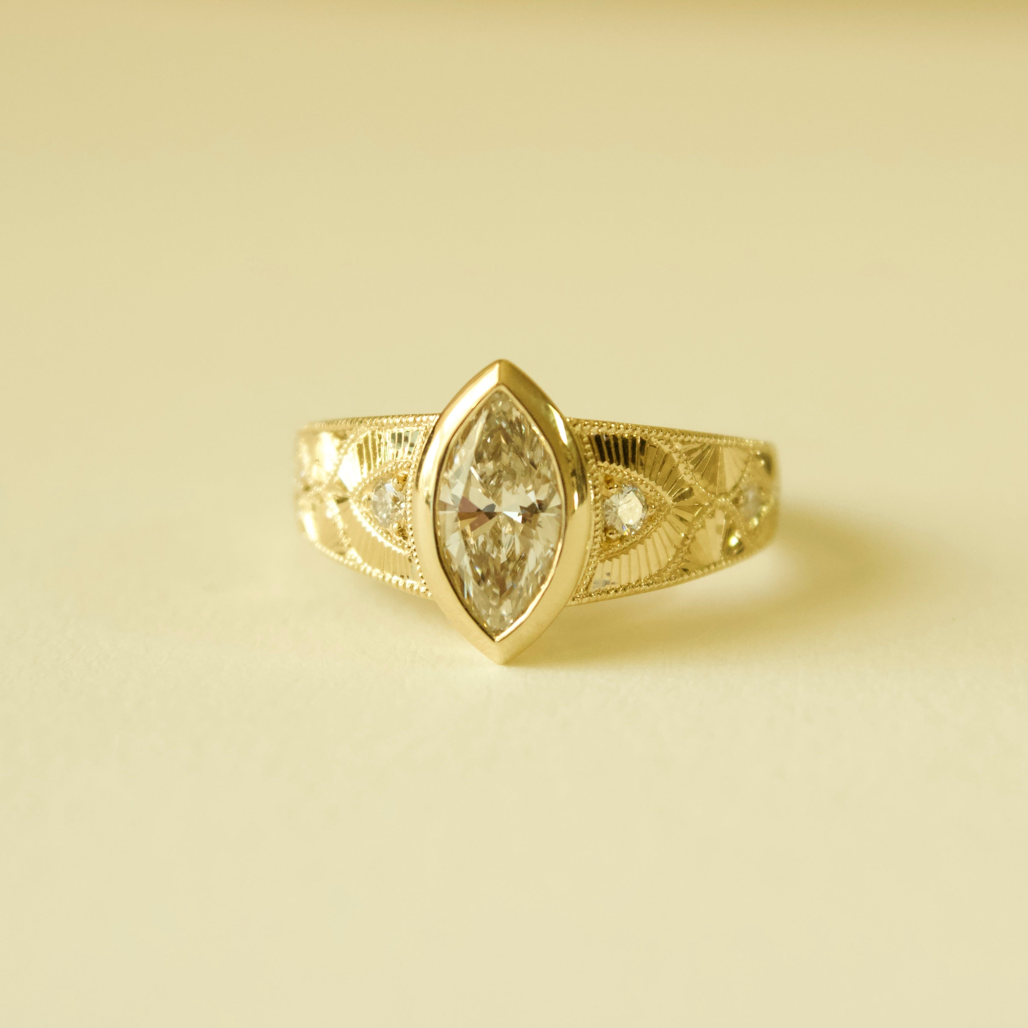 Gold hand engraved bezel marquise ring on a cream background 