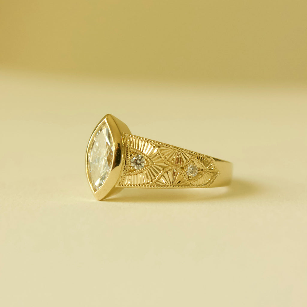 Gold hand engraved bezel marquise ring on a cream background 