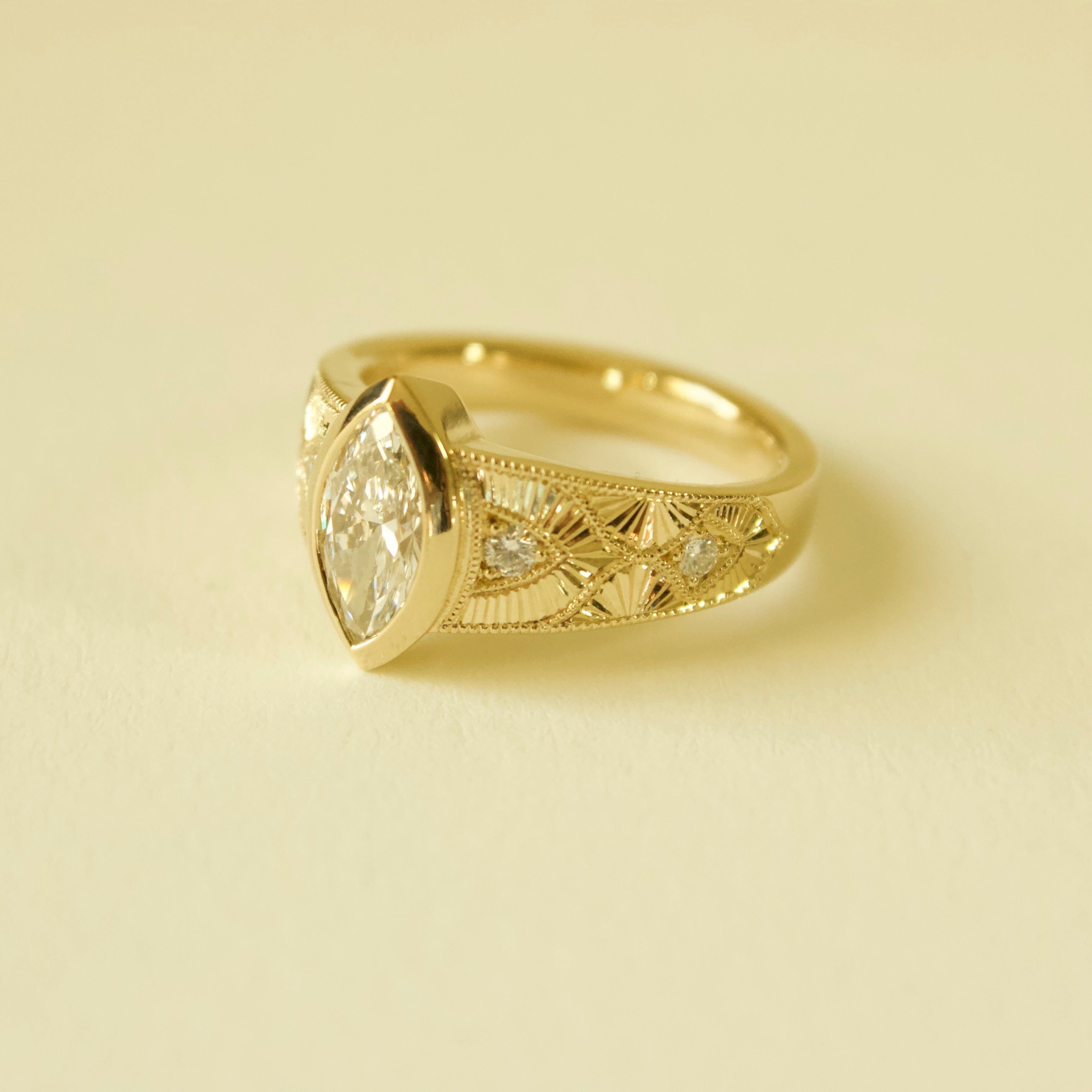 Gold hand engraved bezel marquise ring on a cream background 