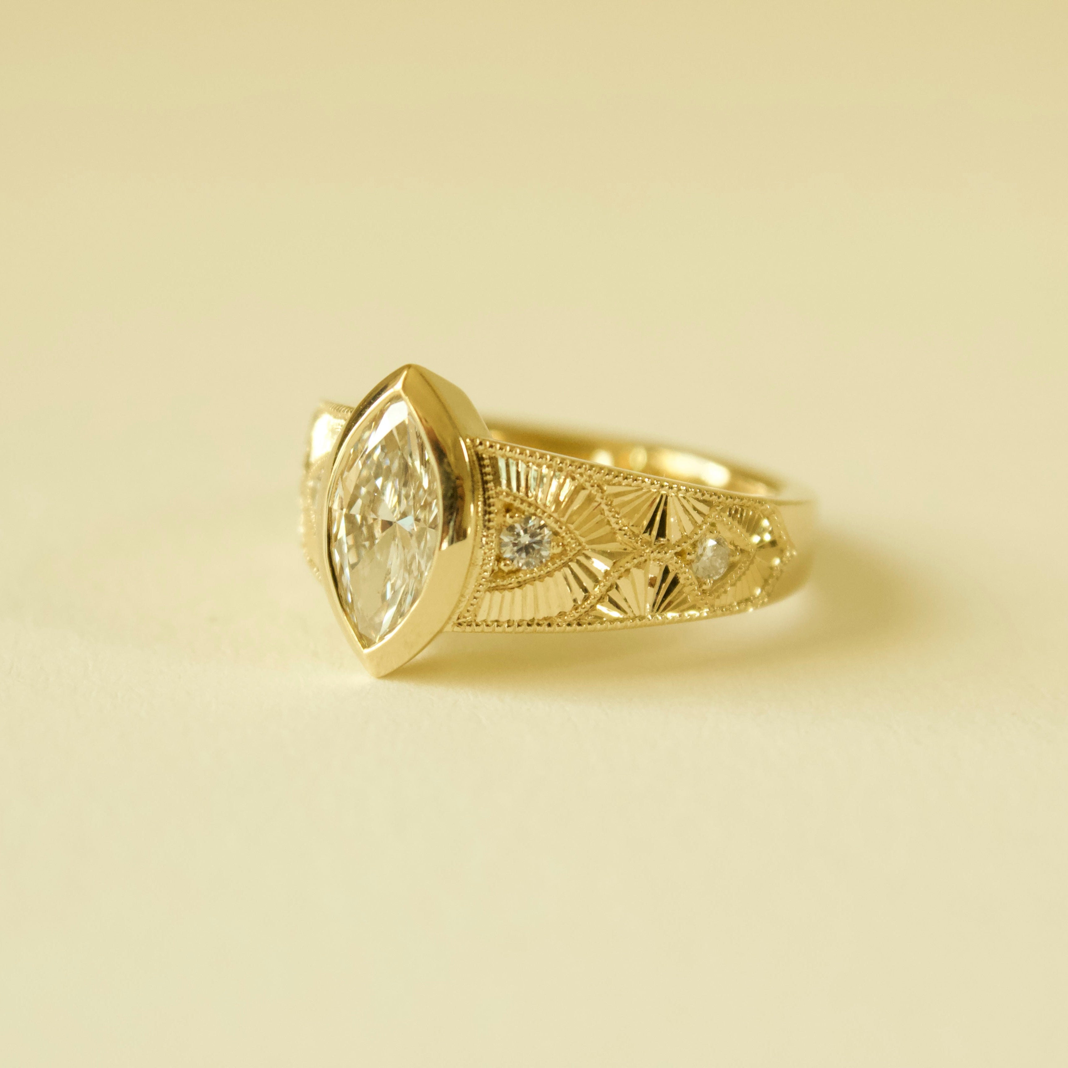Gold hand engraved bezel marquise ring on a cream background 