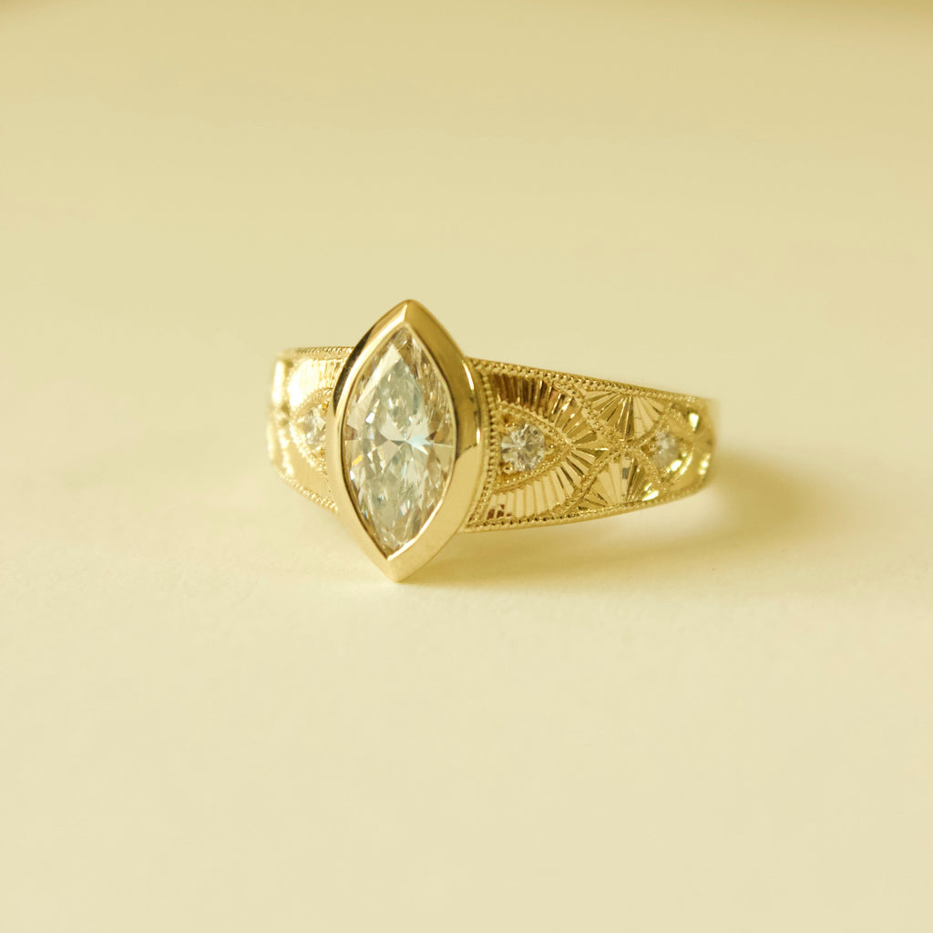 Gold hand engraved bezel marquise ring on a cream background 