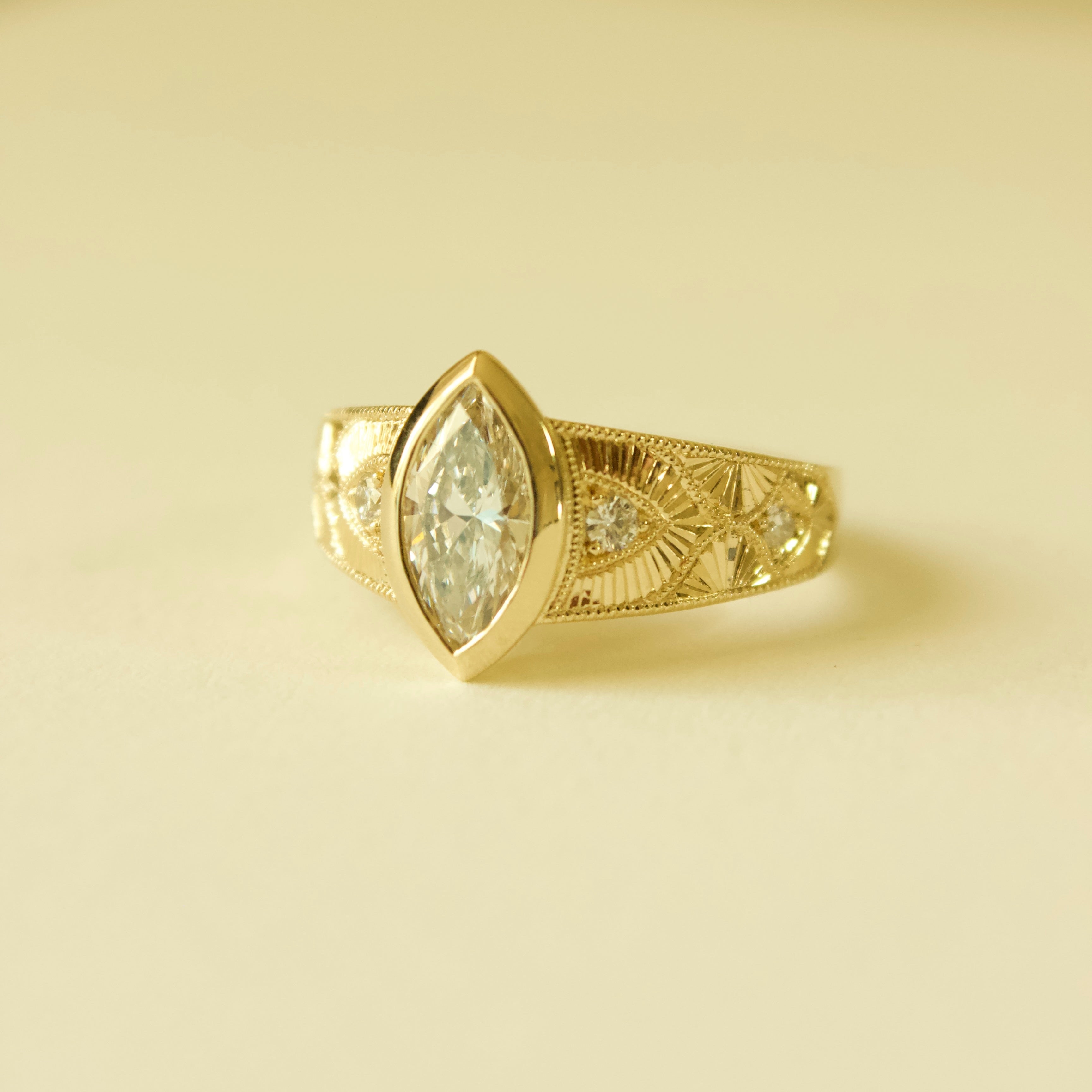 Gold hand engraved bezel marquise ring on a cream background 