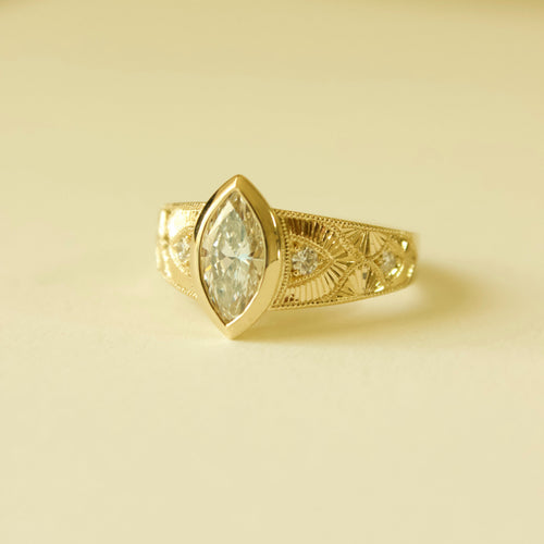 Gold hand engraved bezel marquise ring on a cream background 