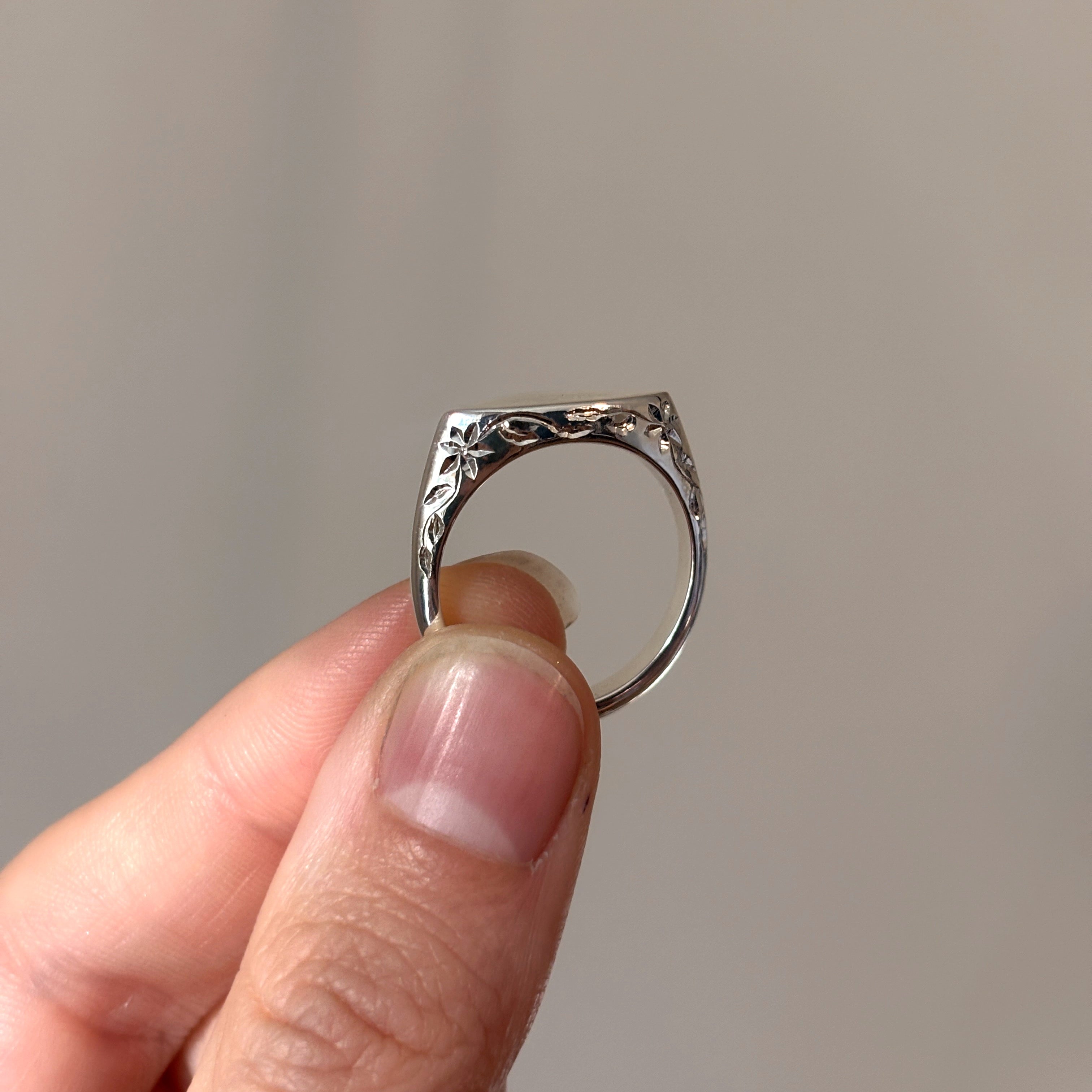 Silver ring held by a hand against a neutral background
