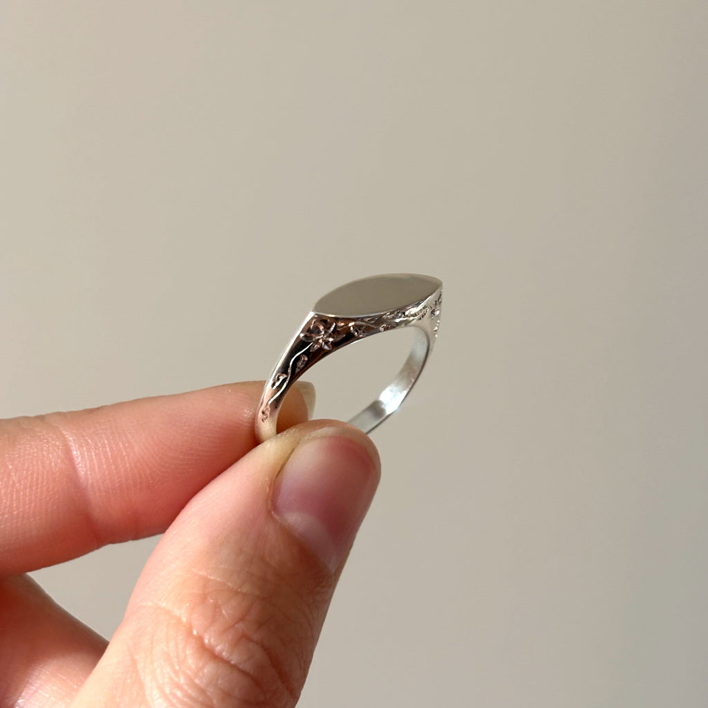 Silver ring held between fingers against a plain background