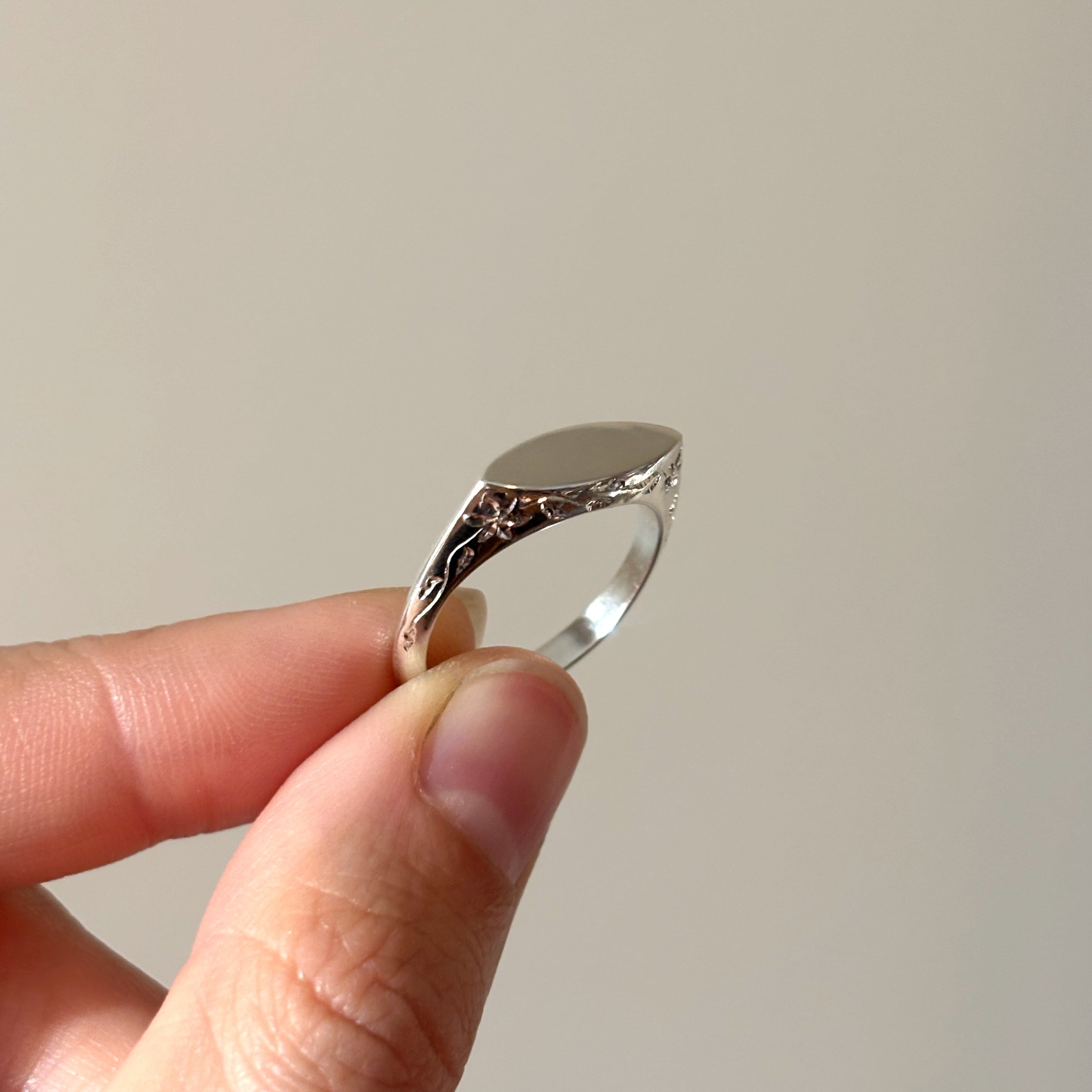 Silver ring held between fingers against a plain background