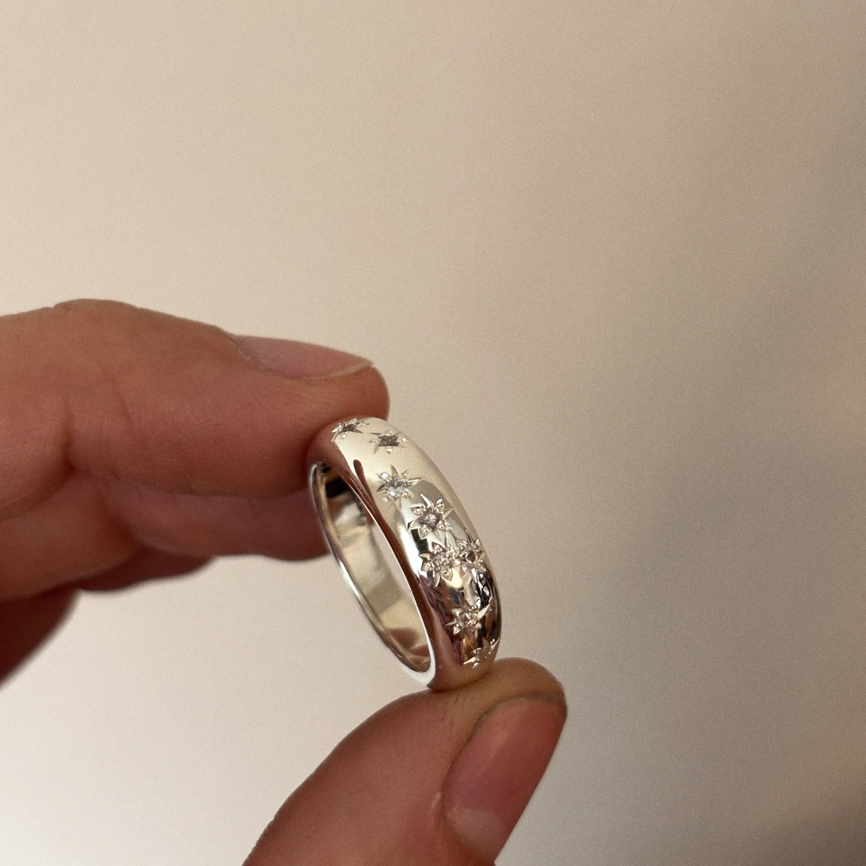 Silver ring held between two fingers against a neutral background